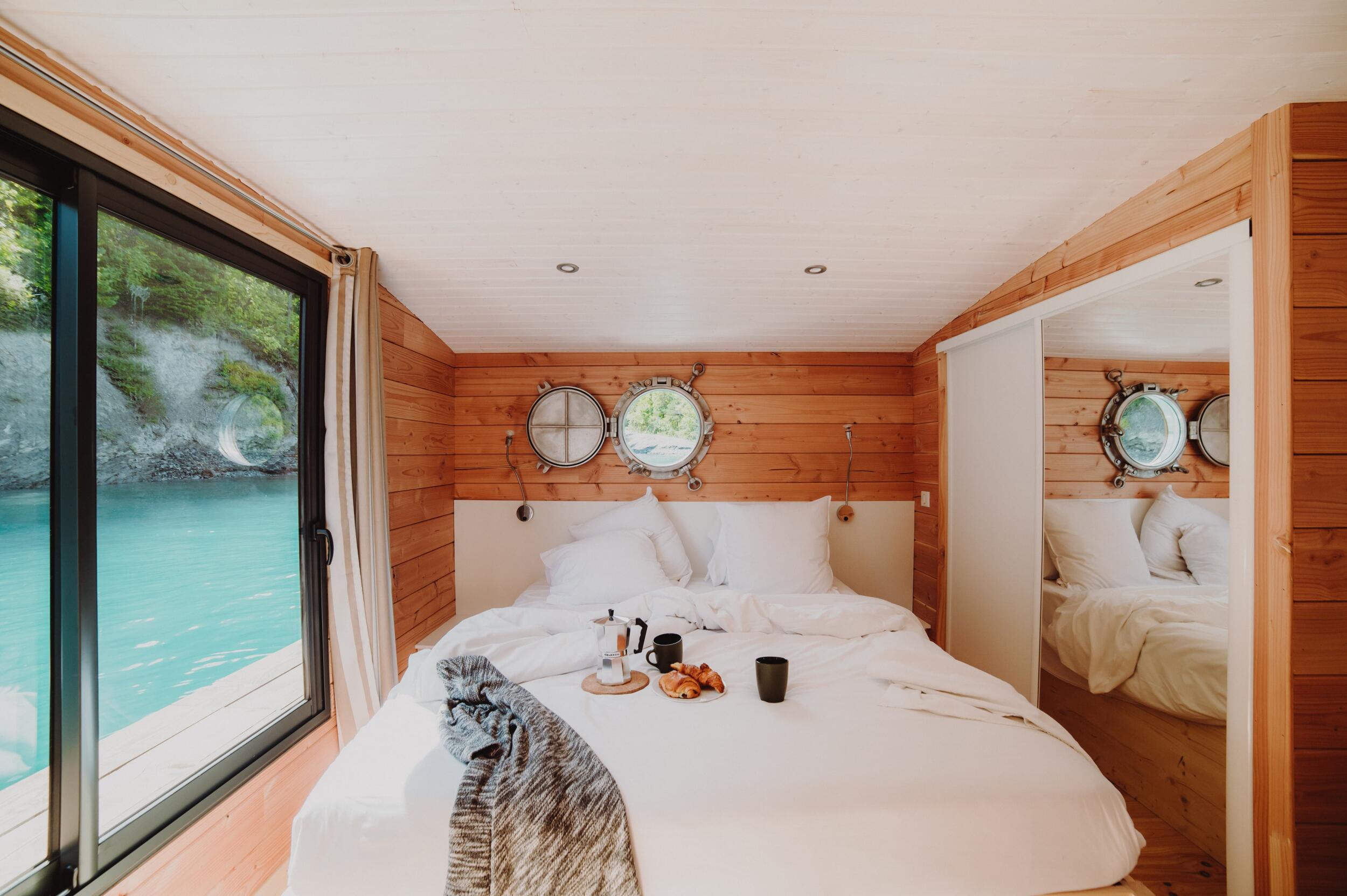 Holzzimmer mit Doppelbett und Blick auf einen türkisfarbenen Fluss von der Unterkunft aus