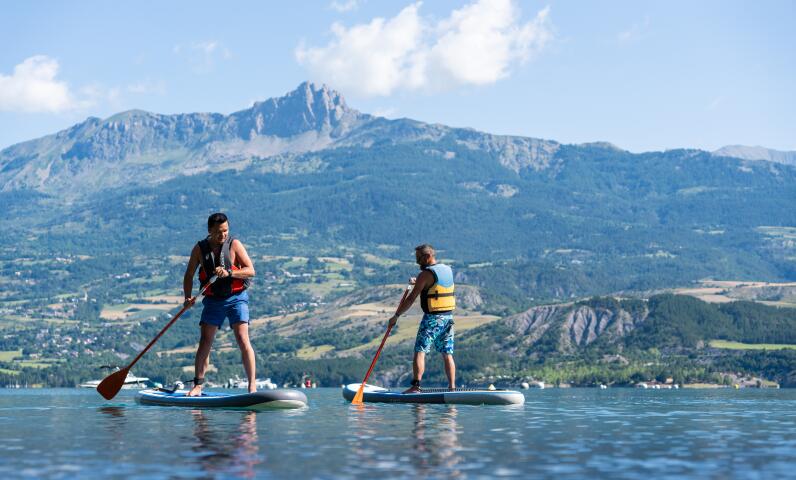 Two people paddleboarding on a mountain lake with views of the peaks