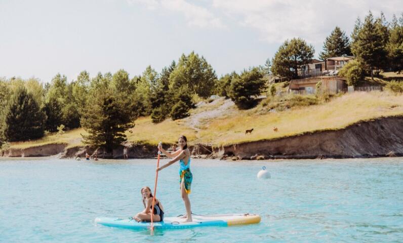 Niños en una tabla de paddle surf en medio de un lago de montaña en verano